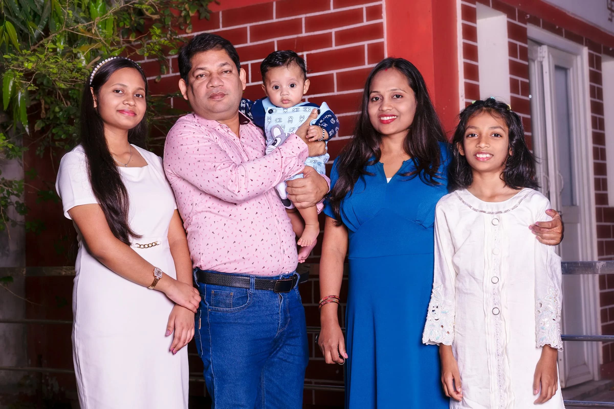 Family of five with a baby posing in front of their home