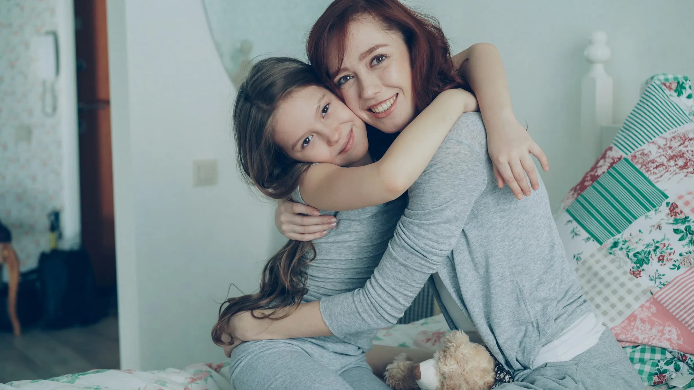 Mother and daughter smiling in a hug in their bedroom at home